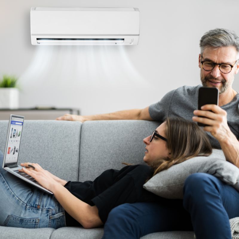couple on devices on sofa with wall mounted air conditioning on in the background