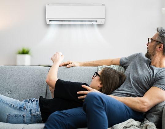 people on sofa operating wall mounted air conditioner with remote control