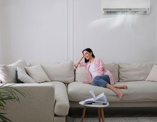 woman on sofa enjoying air conditioning from wall mounted unit