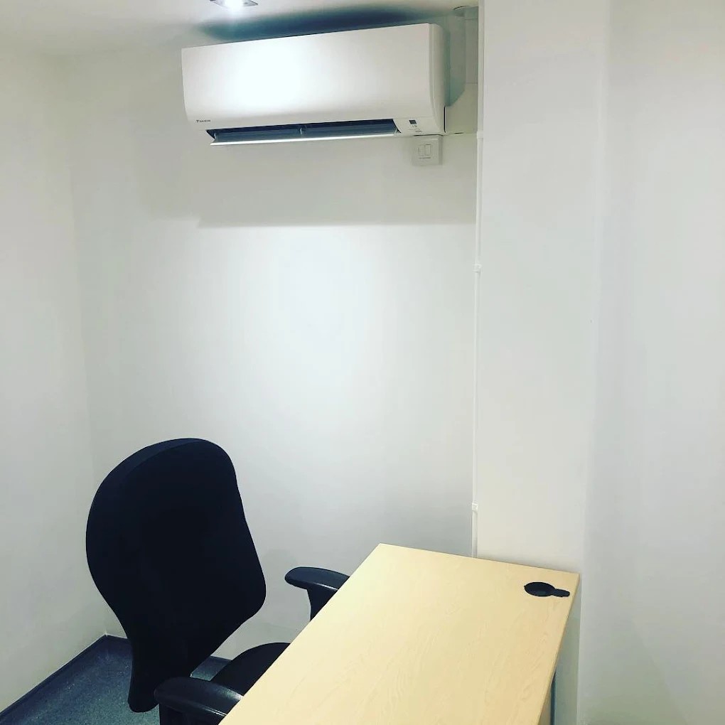 wall mounted air conditioner installed in room with a single office chair and desk